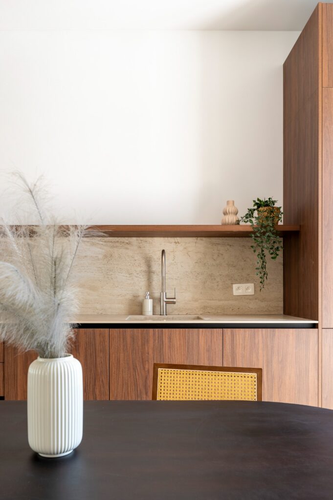 Notelaar keukenkasten met wandplank en planten tegen travertinlook achterwand, projectkeuken in Antwerpen